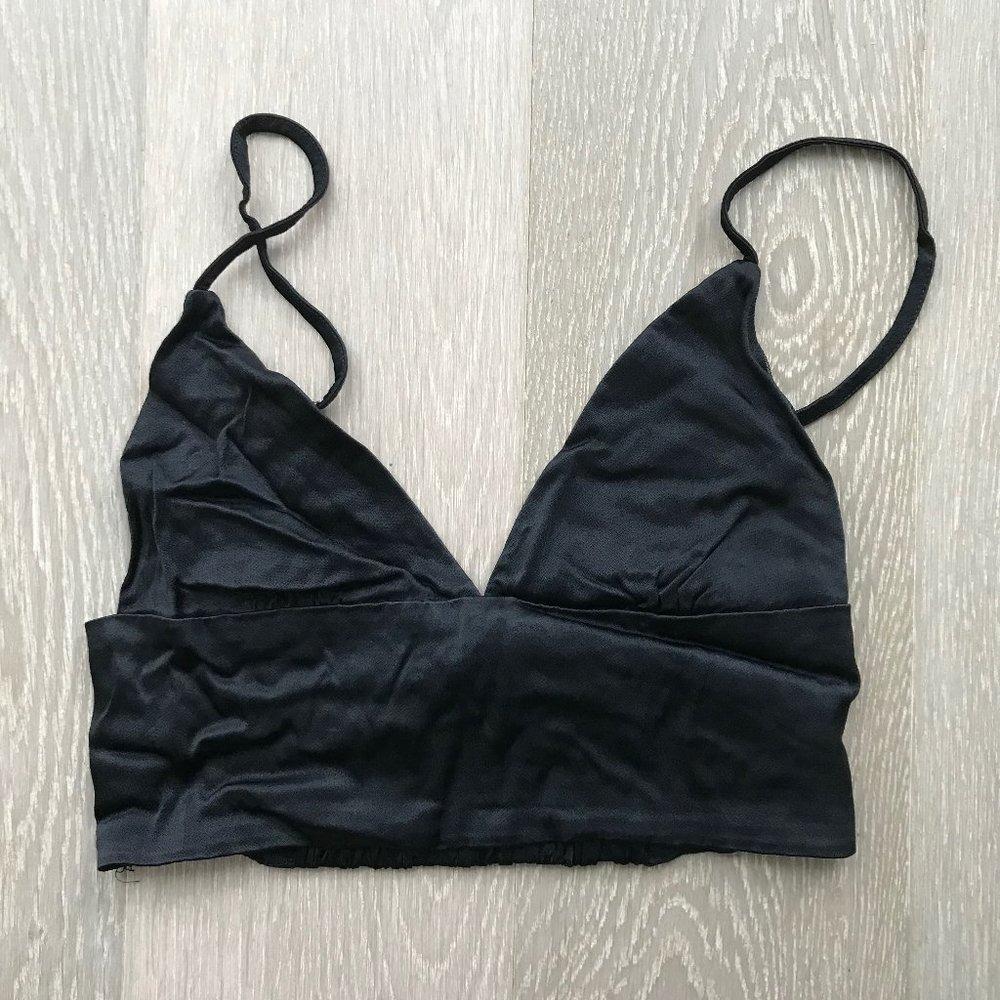 Black bralette with thin straps and a V-neck, with an elastic band at the bottom, on a light wood surface.