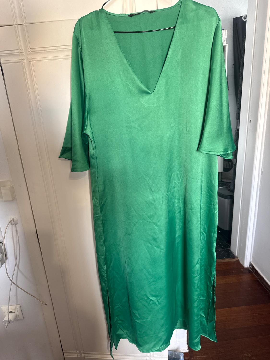 Green satin dress with a V-neck and three-quarter sleeves, hanging on a hanger over a white door.