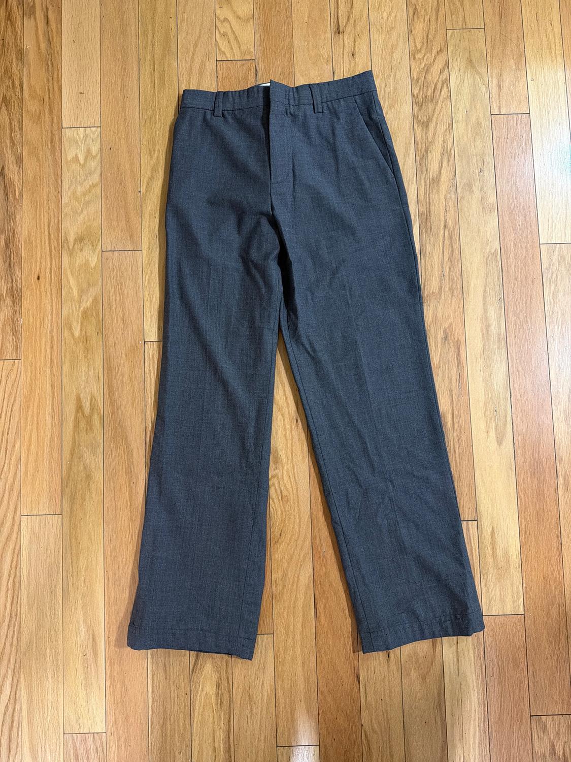Gray dress pants placed on a light wooden floor, showcasing a classic design with pockets and belt loops.