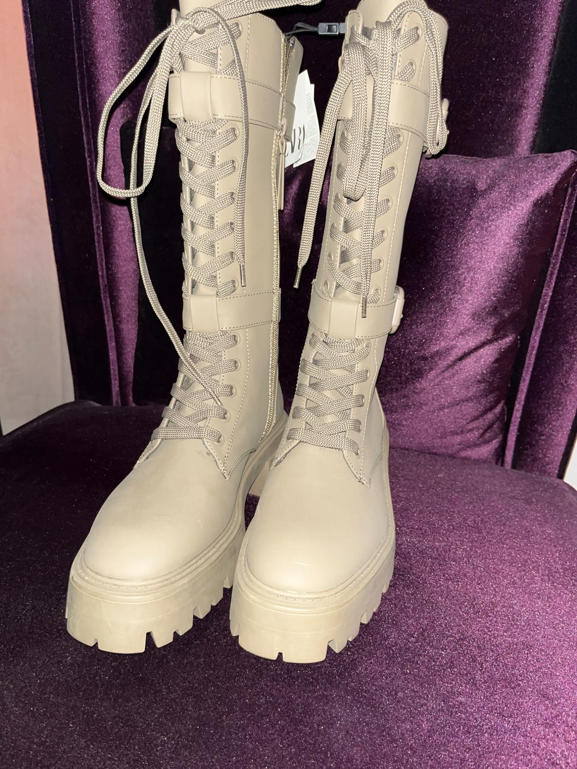 Beige high-laced boots on a purple velvet armchair. Visible tag hanging from one boot.
