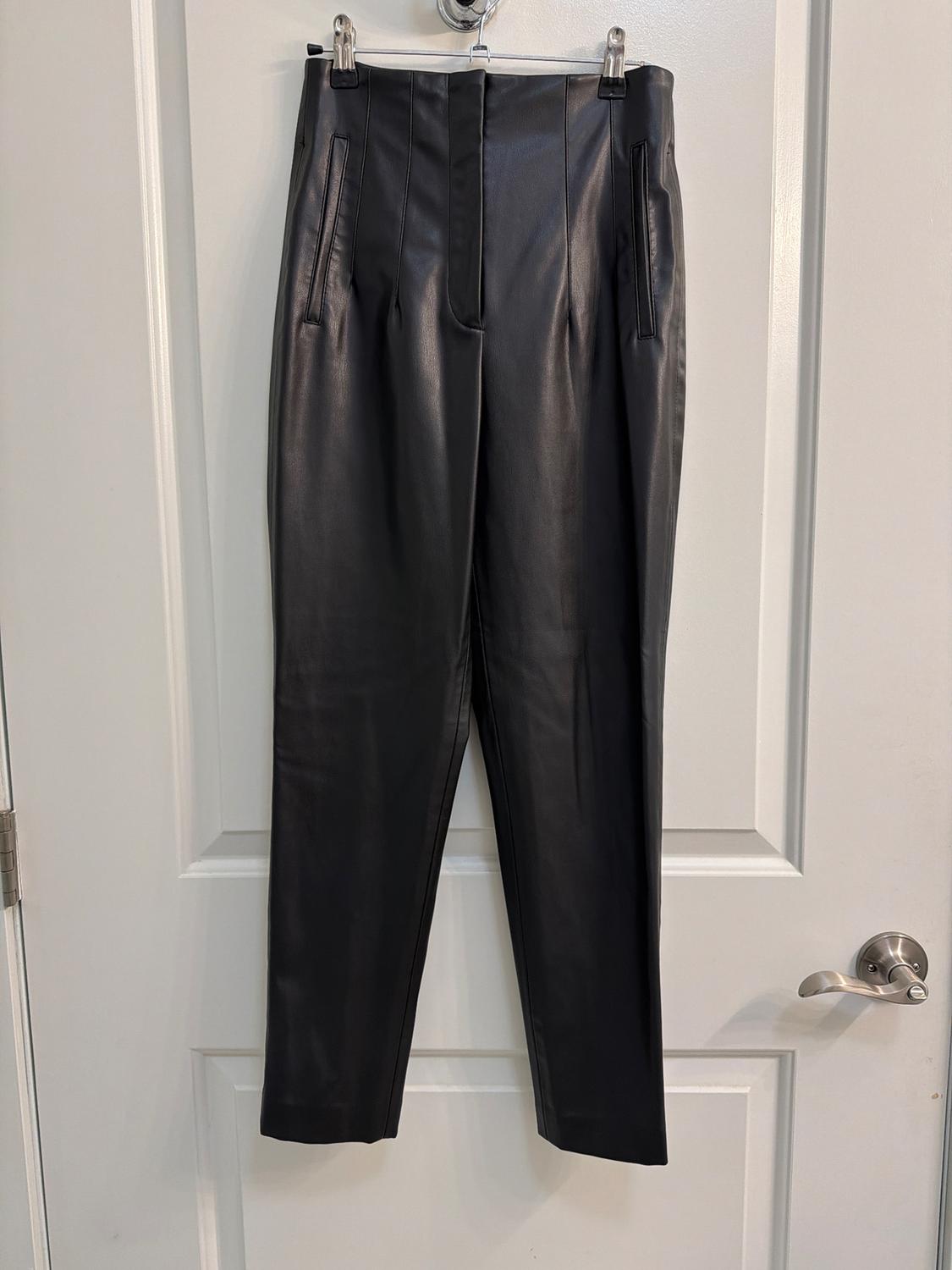 Black pants hanging on a white door, with side pockets and pleats at the waist, elegant and modern style.