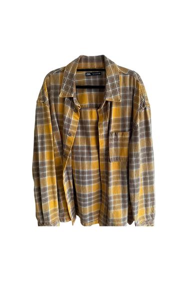 Brown and yellow checked shirt with chest pocket, hanging against a white background. Visible label on the collar.