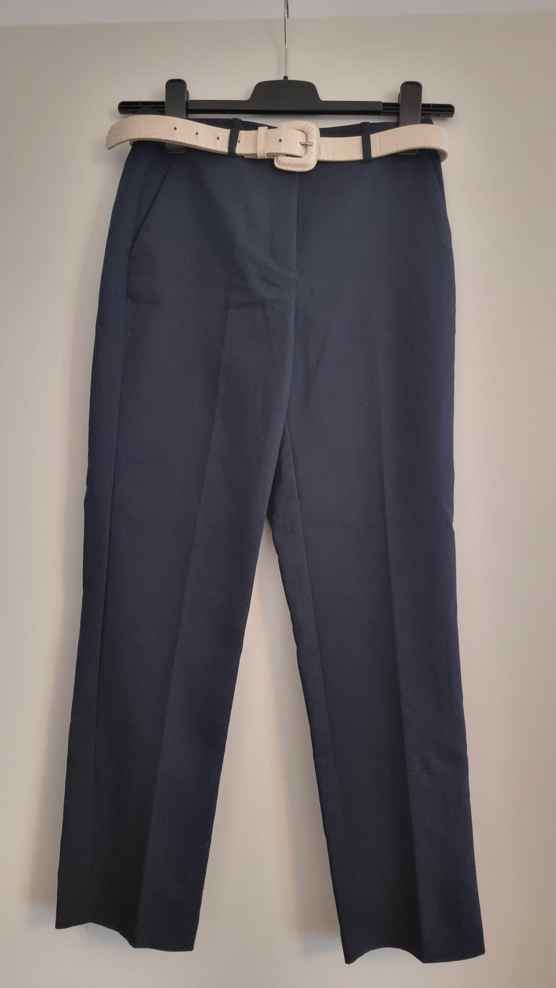 Black trousers hanging on a black hanger with a beige belt. Neutral background.