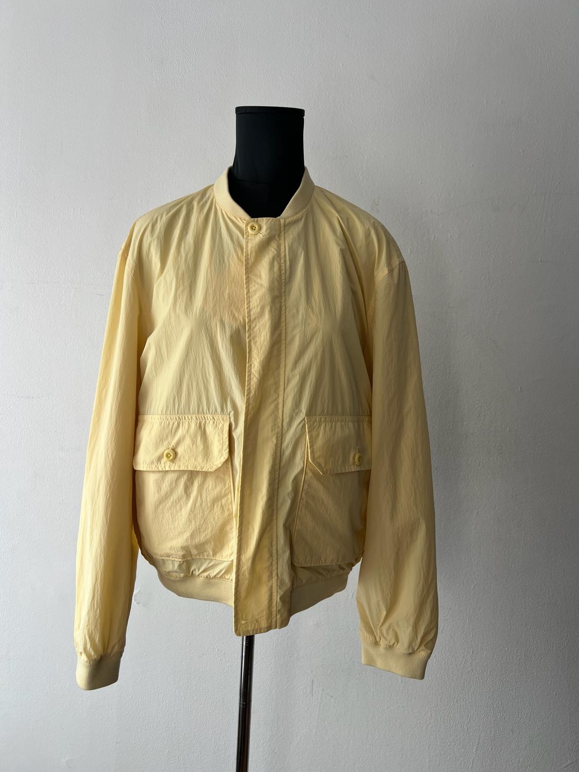 Yellow jacket with front pockets and a button closure, displayed on a black mannequin in front of a white wall.