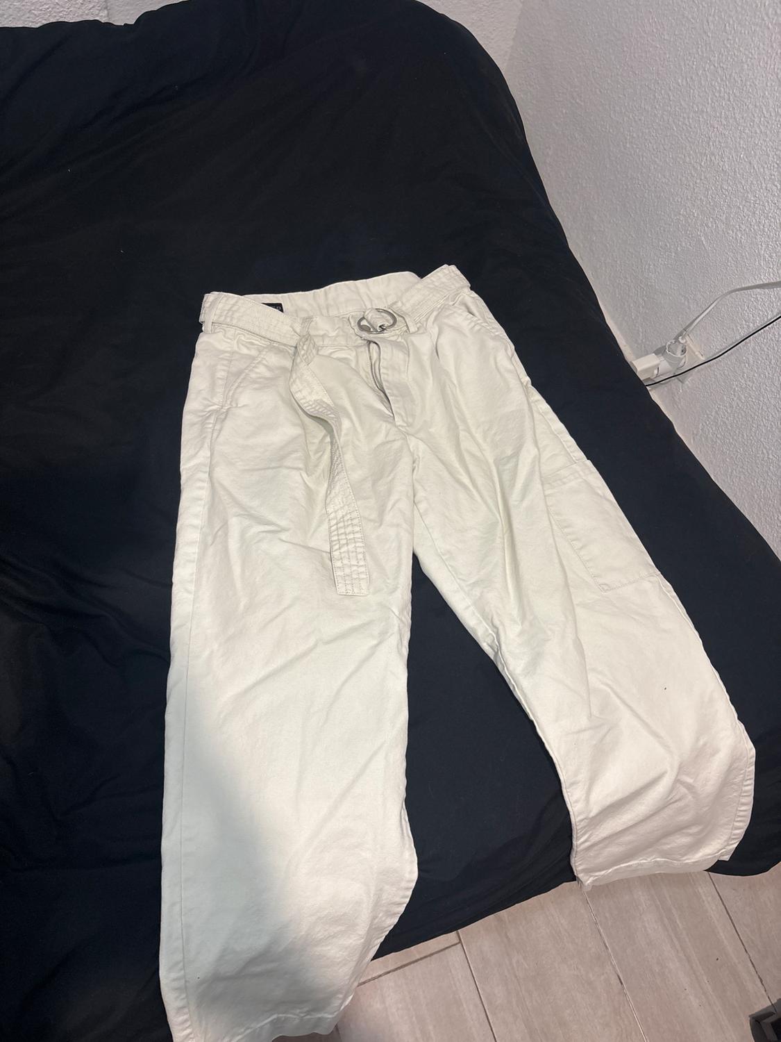 White trousers with a belt on a black bed, in a room with white walls and a light wooden floor.