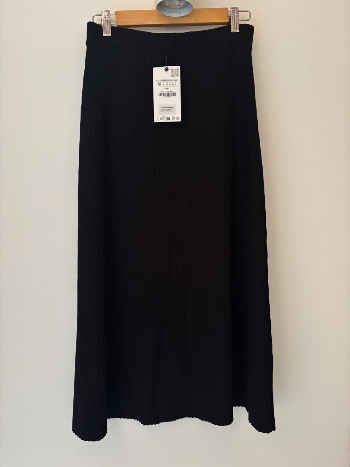 Black ribbed fabric skirt hanging on a wooden hanger, with a visible label indicating size M and a price of €25.99.