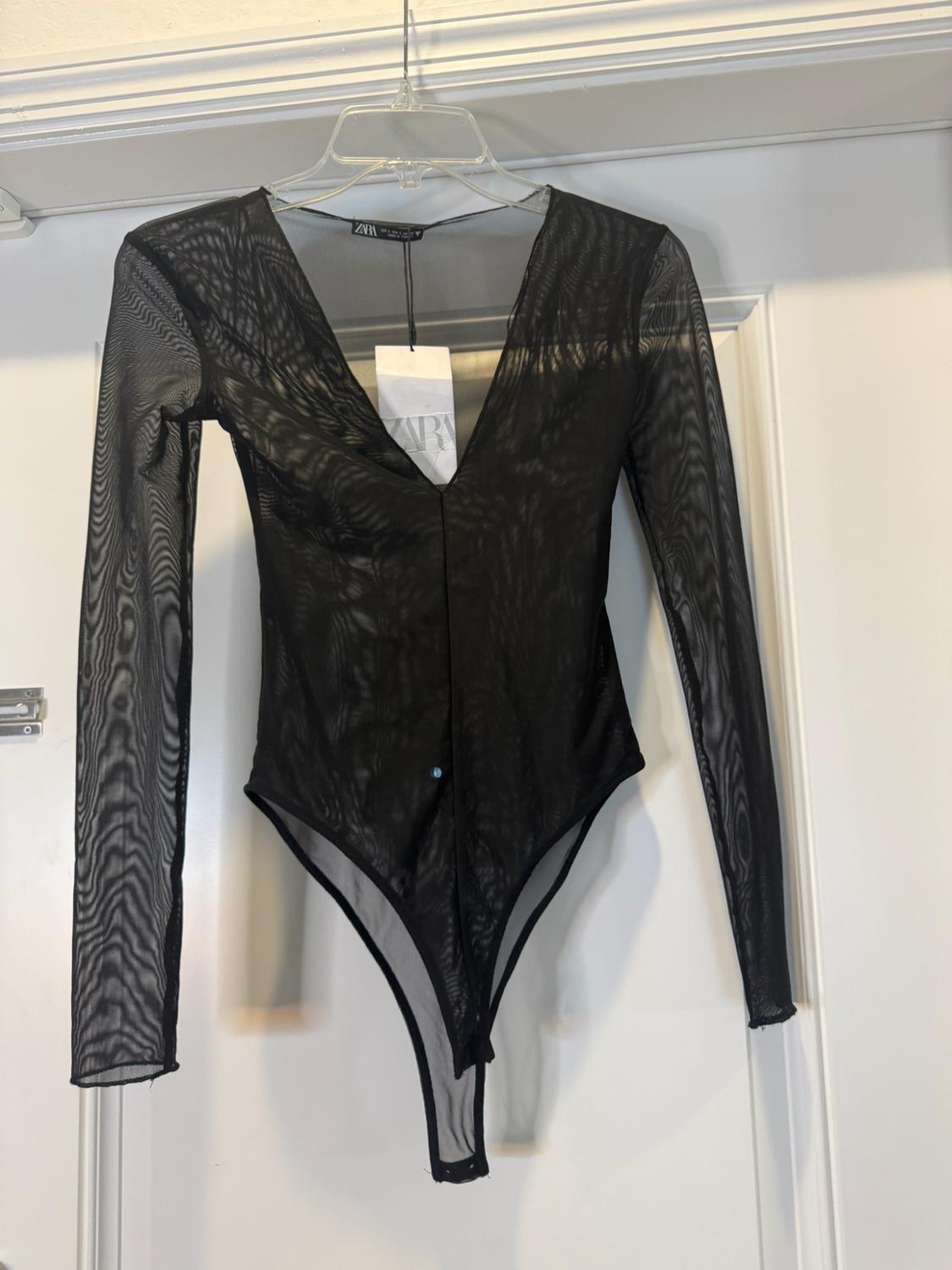 Black semi-sheer long-sleeved V-neck bodysuit, hanging on a hanger on a white door. Label with the text ZARA.