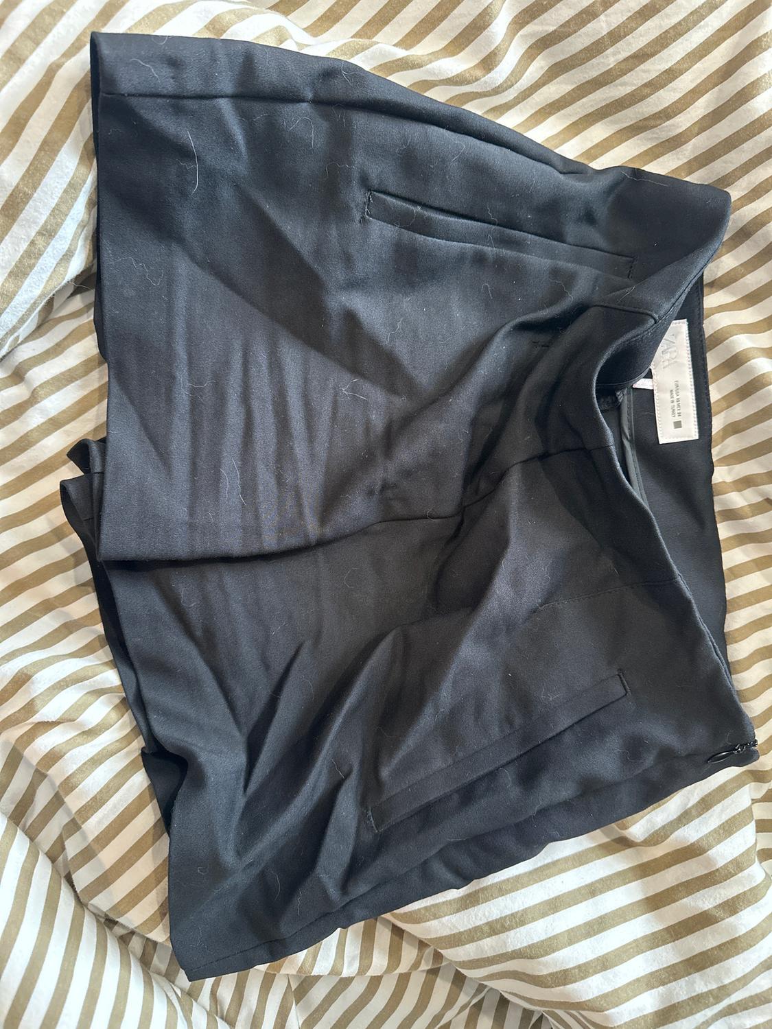 Black shorts on a beige and white striped comforter. Label visible inside the garment.