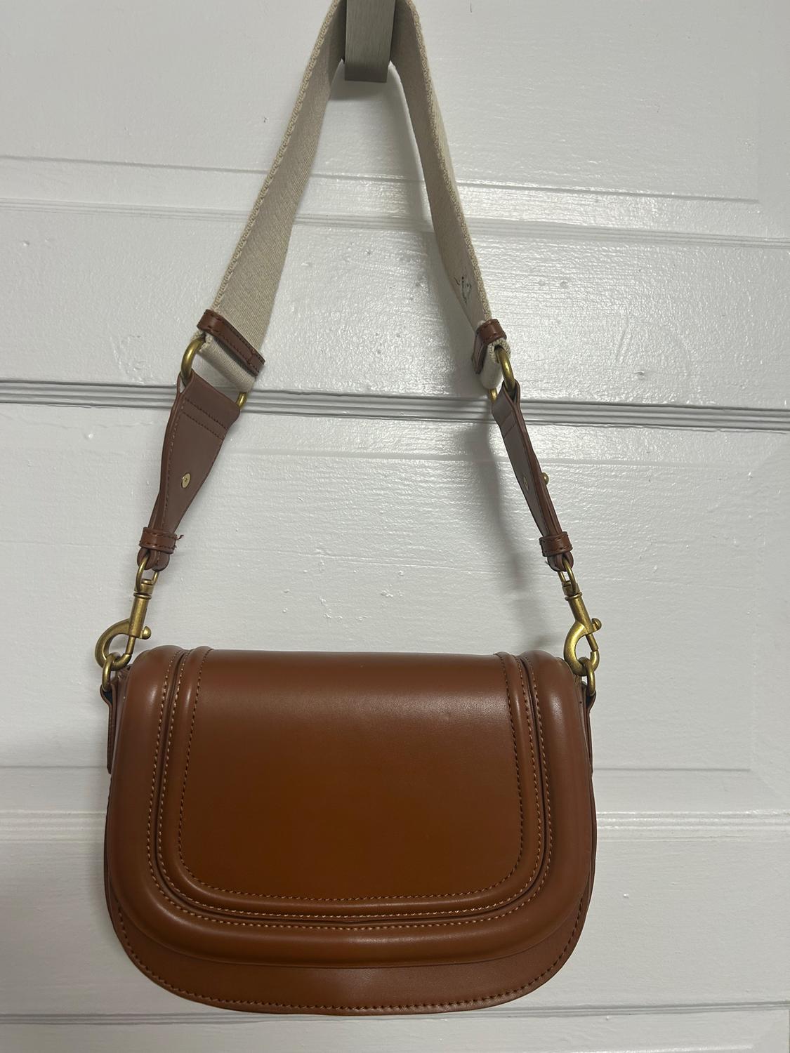 Brown handbag hanging on a white door, with an adjustable beige strap and gold metallic details.