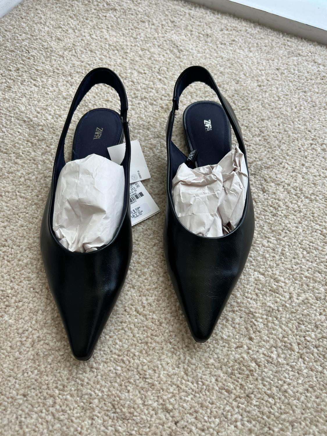 Top view of black pointed-toe slingback flats with a tag on a light-coloured rug. Text: ZARA.