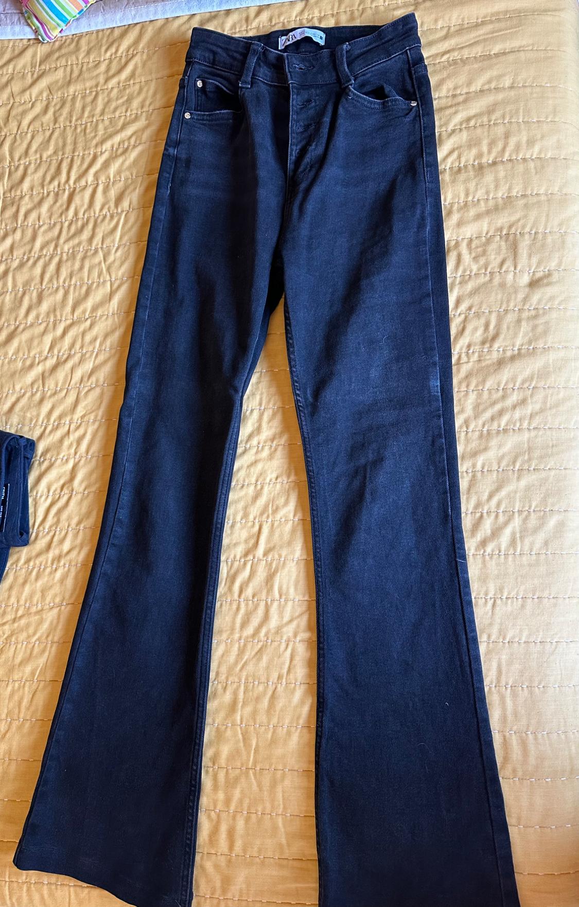 Dark, flared denim jeans with a ZARA label, laid out on a yellow quilted bedspread. Casual and relaxed style.