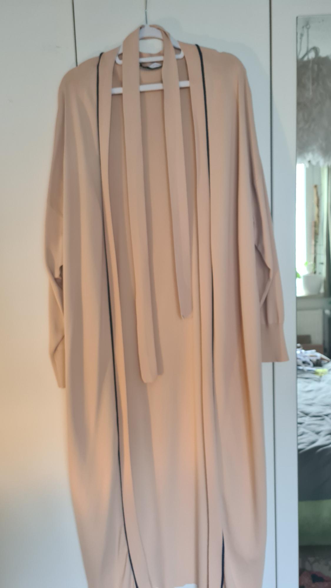 Beige dress hanging on a hanger, with black lines down the sides, reflected in a bedroom mirror.