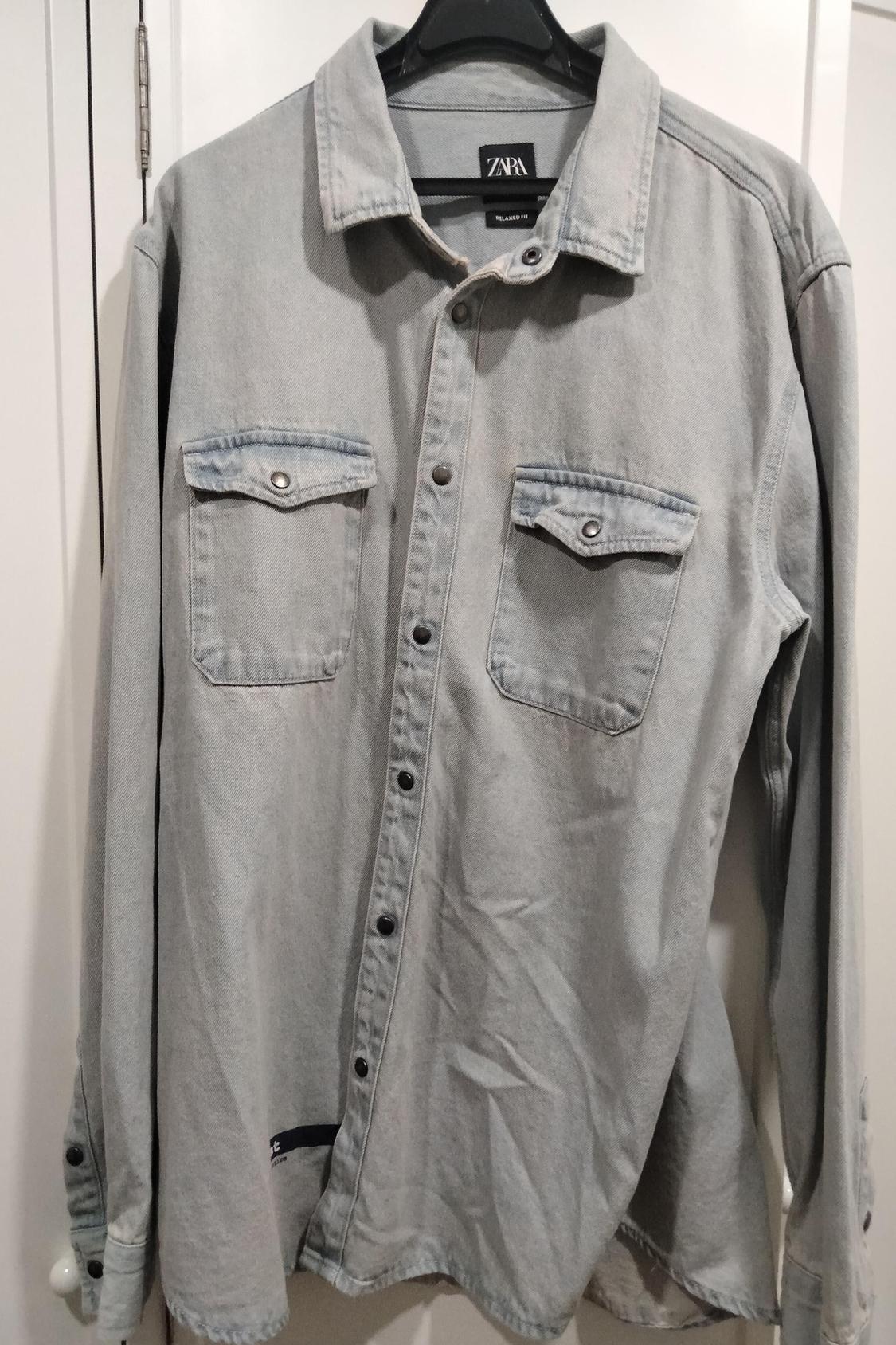 Front view of a grey shirt with front flap pockets and black buttons.