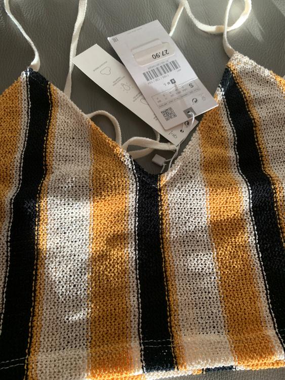 Strap top woven with black, white, and mustard stripes, with visible tags. Price: 27.90. Gray background.