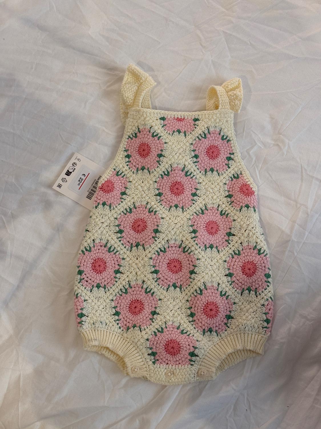 Crochet playsuit in cream tones with pink and green flowers. Visible label with price of 22.95. White fabric background.
