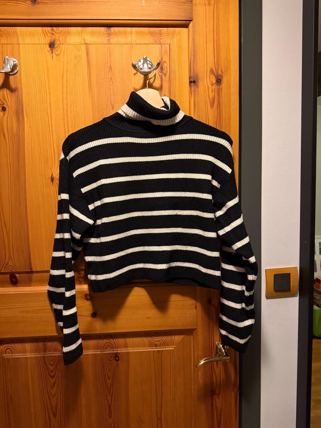 Black-and-white striped roll-neck jumper hanging on a hanger over a wooden door. Casual, homely atmosphere.