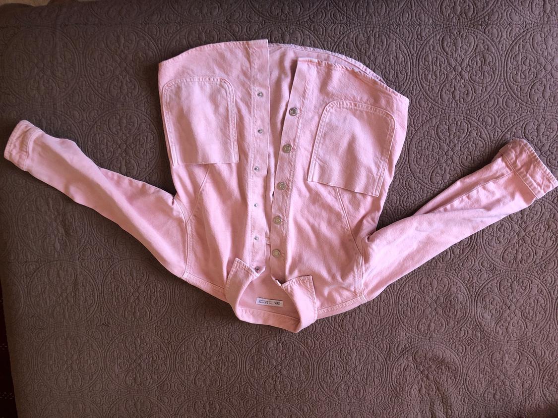 Light pink shirt with buttons and two front pockets, spread out on a grey bedspread with an embossed circular design.