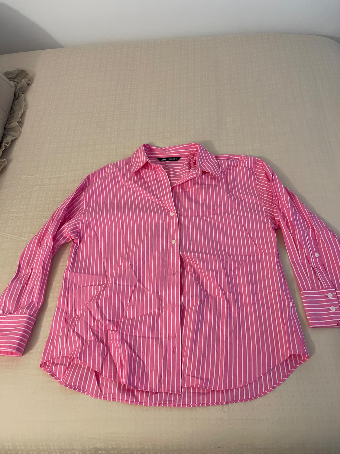 White and pink vertical striped shirt on a beige bed. Long sleeves with buttoned cuffs and a classic collar.