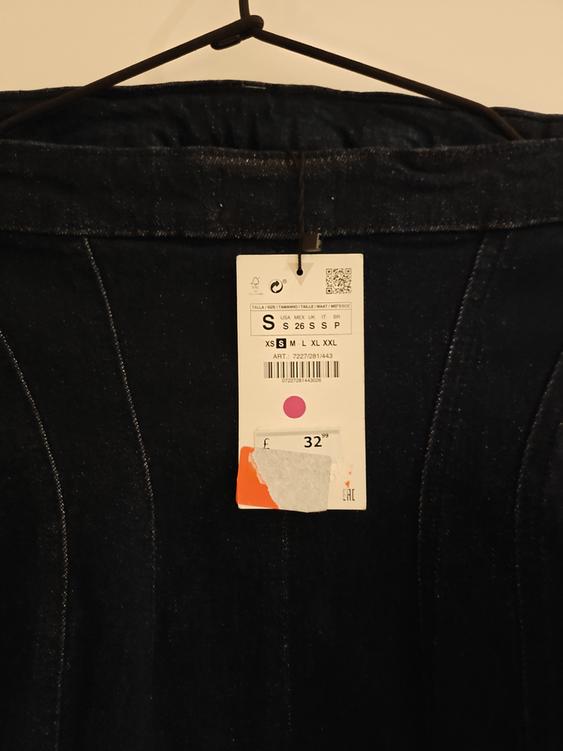 Dark blue denim jeans label on hanger, showing size S and price £32.99. White background, visible stitching details.