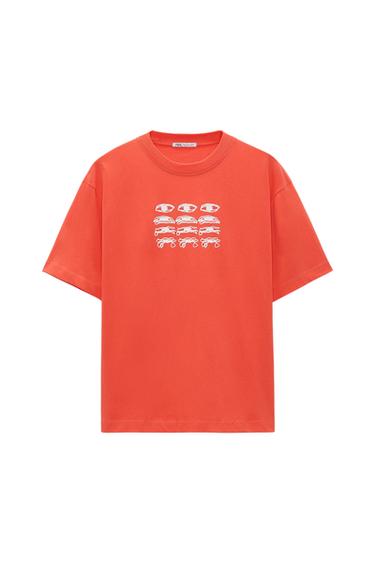 Front view of an orange t-shirt with a graphic print of eyes and cars on the chest