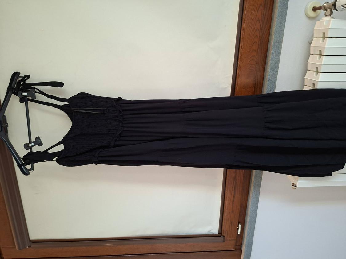 A long black dress hangs on a hanger in front of a wooden door. The fabric is light and has thin straps.