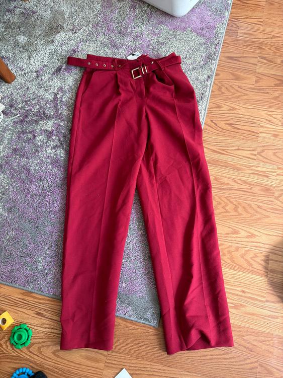 Red pants with a belt on a gray rug and wooden floor. Colorful toys in the bottom left corner.