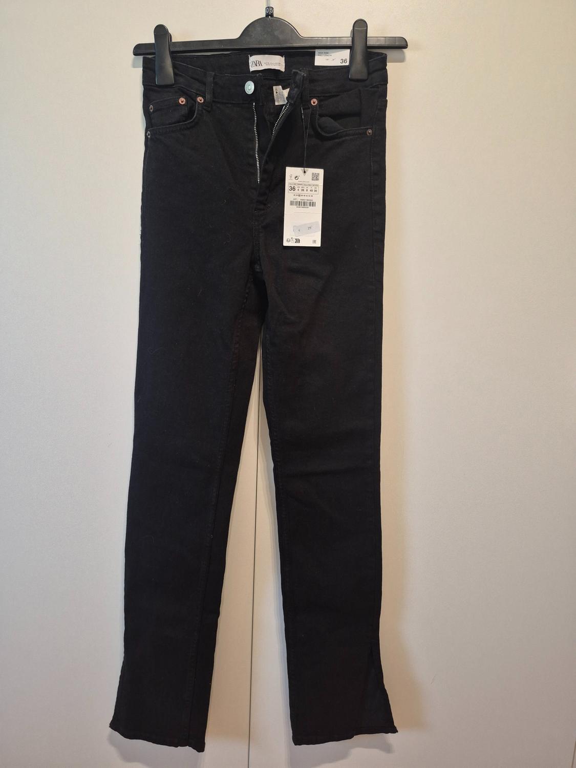 Black trousers hanging on a hanger with a visible tag. Plain white background. Size 36.