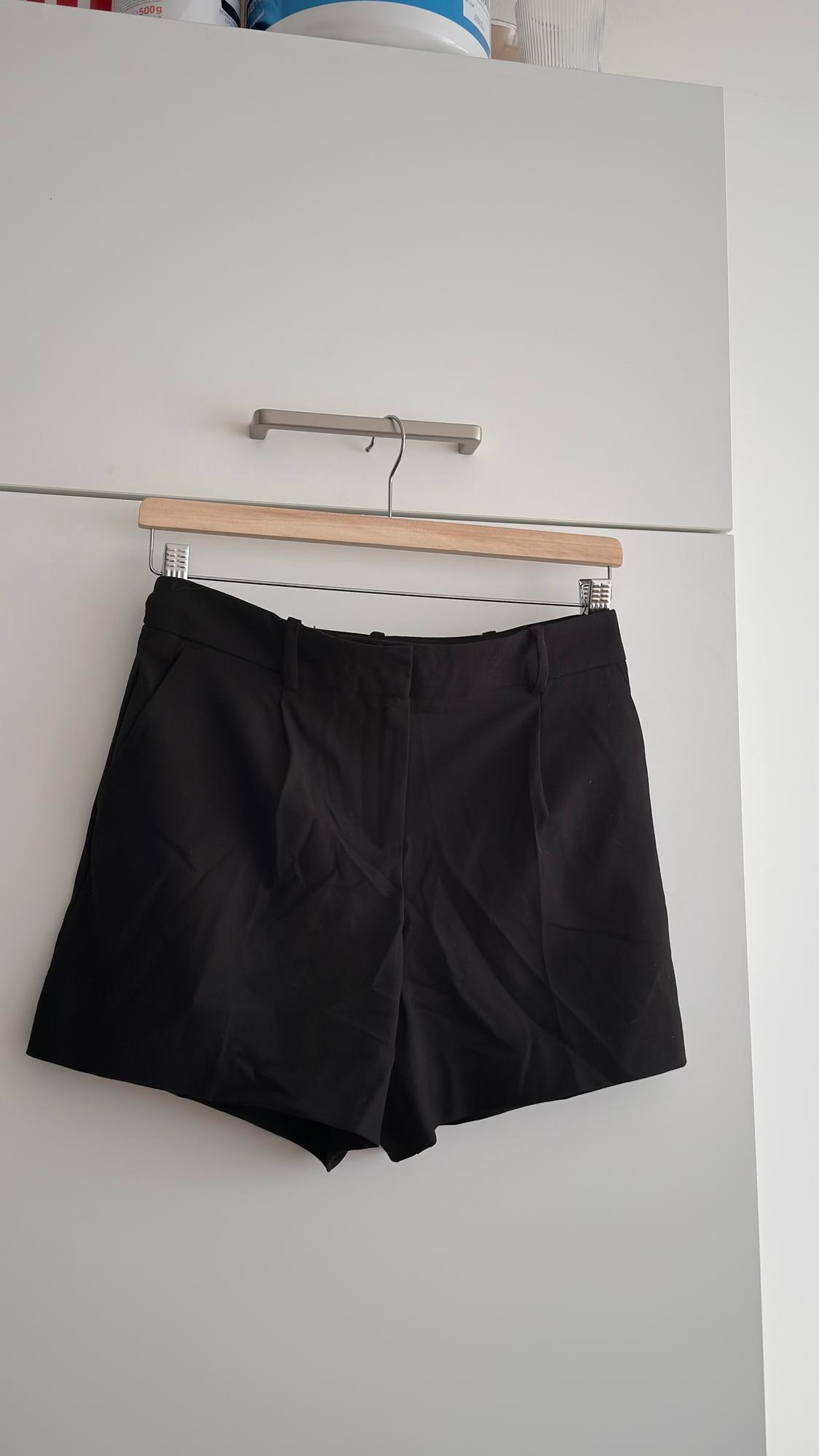Black shorts hanging on a wooden hanger in front of a white wardrobe. Top of the wardrobe visible.