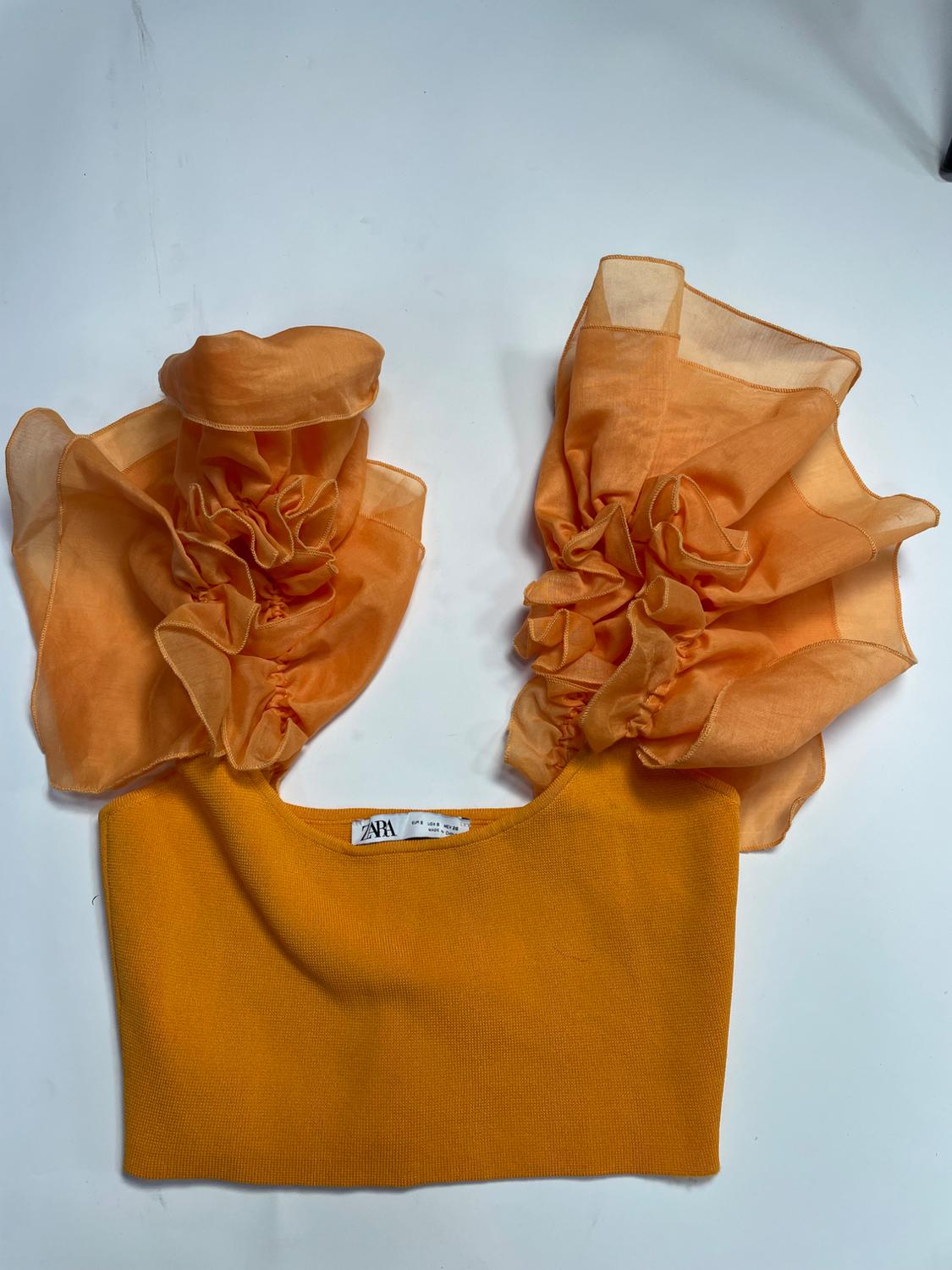 Orange top with a knitted body and voluminous frilled sleeves against a white background. Label with the text ZARA.