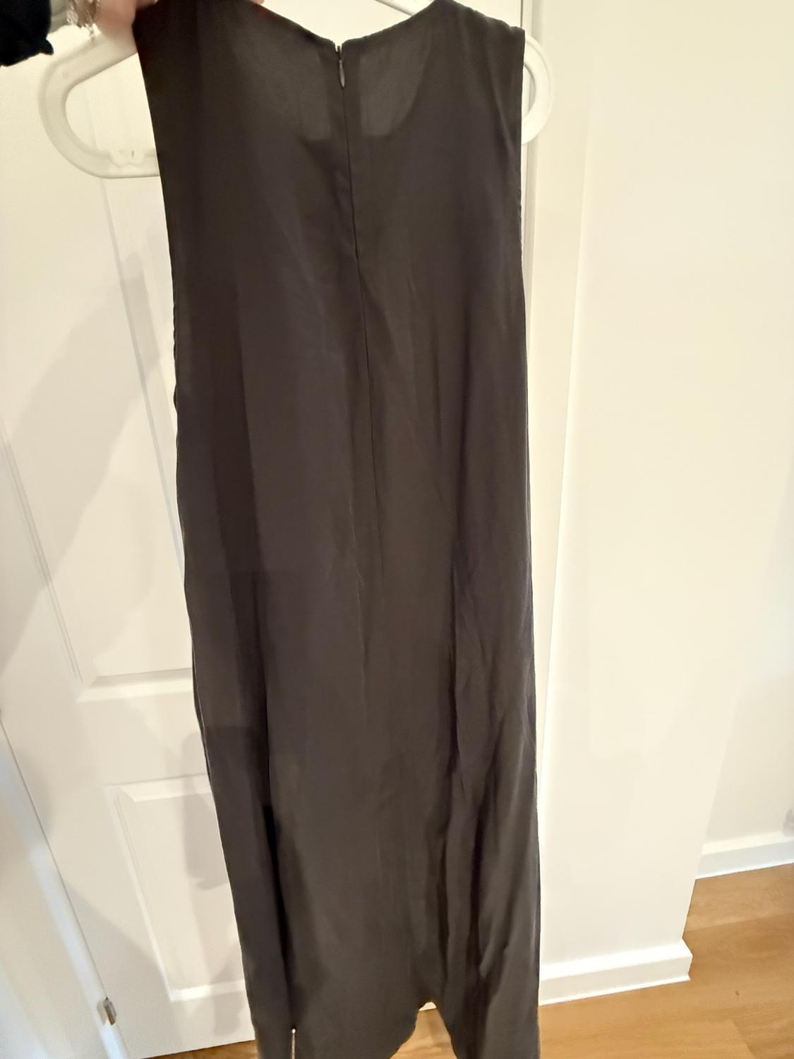 Hand holding a hanger with a long dark sleeveless dress in front of a white door.