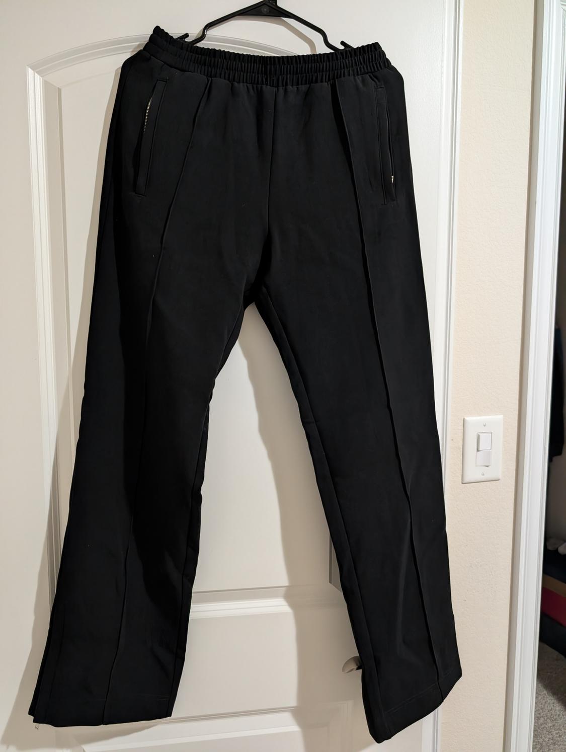 Black trousers hanging on a hanger over a white door. They have an elasticated waist and zipped pockets.