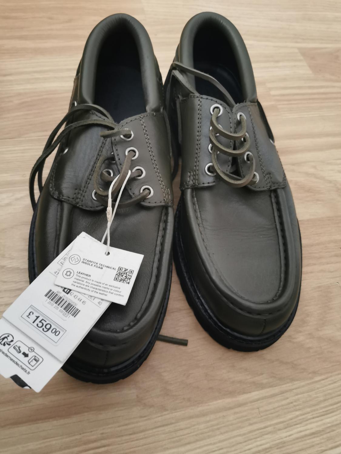 Black leather laced shoes on a wooden floor. Visible tag with price of £159.00 and QR code.