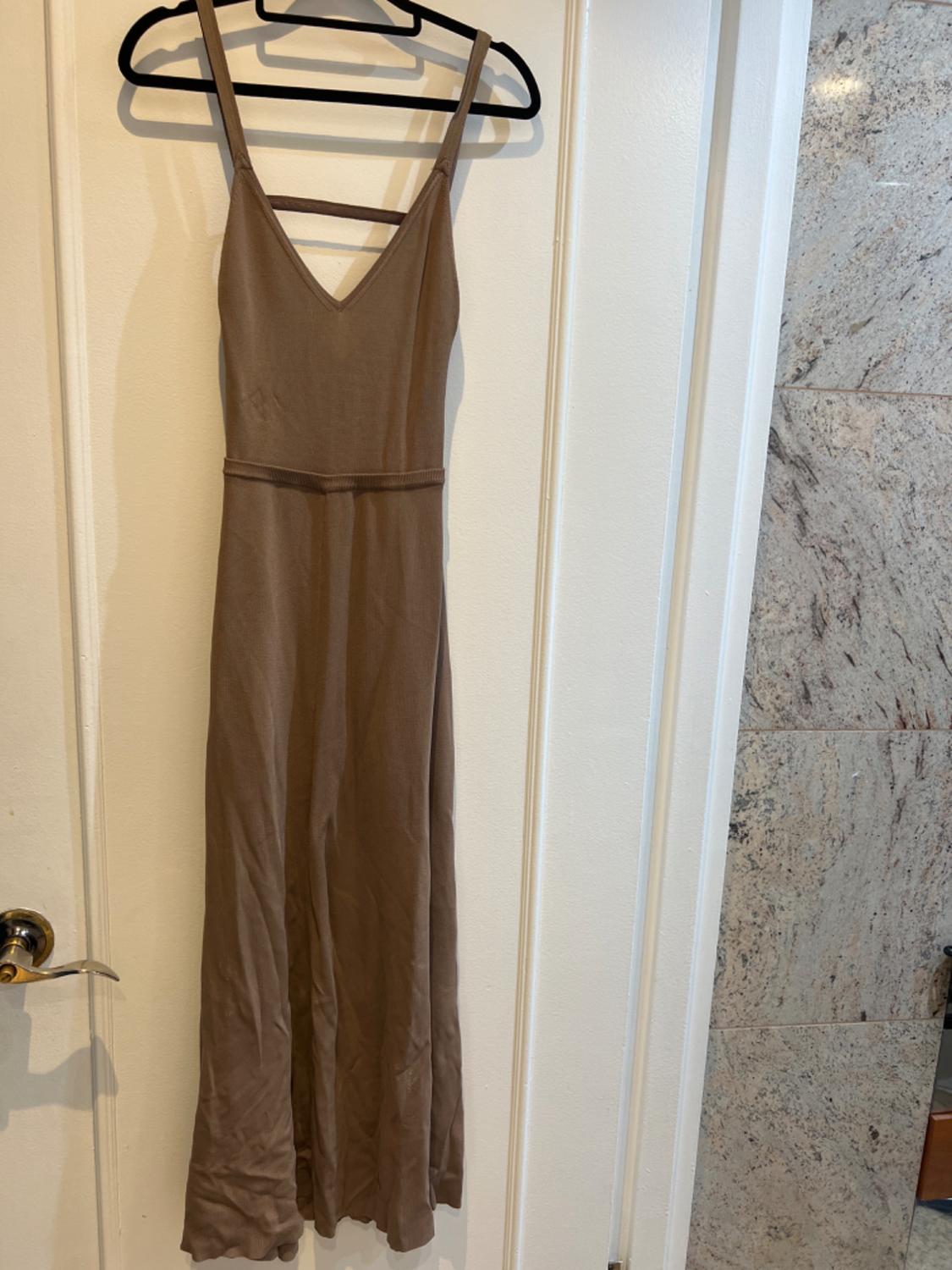 Long brown sleeveless dress hanging on a black hanger over a white door, with a marble wall background.