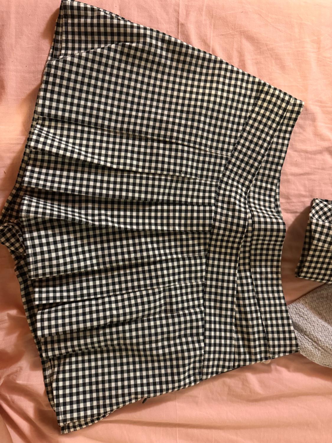 Short pleated skirt in a black and white check print, laid on crumpled pink fabric. Casual style.