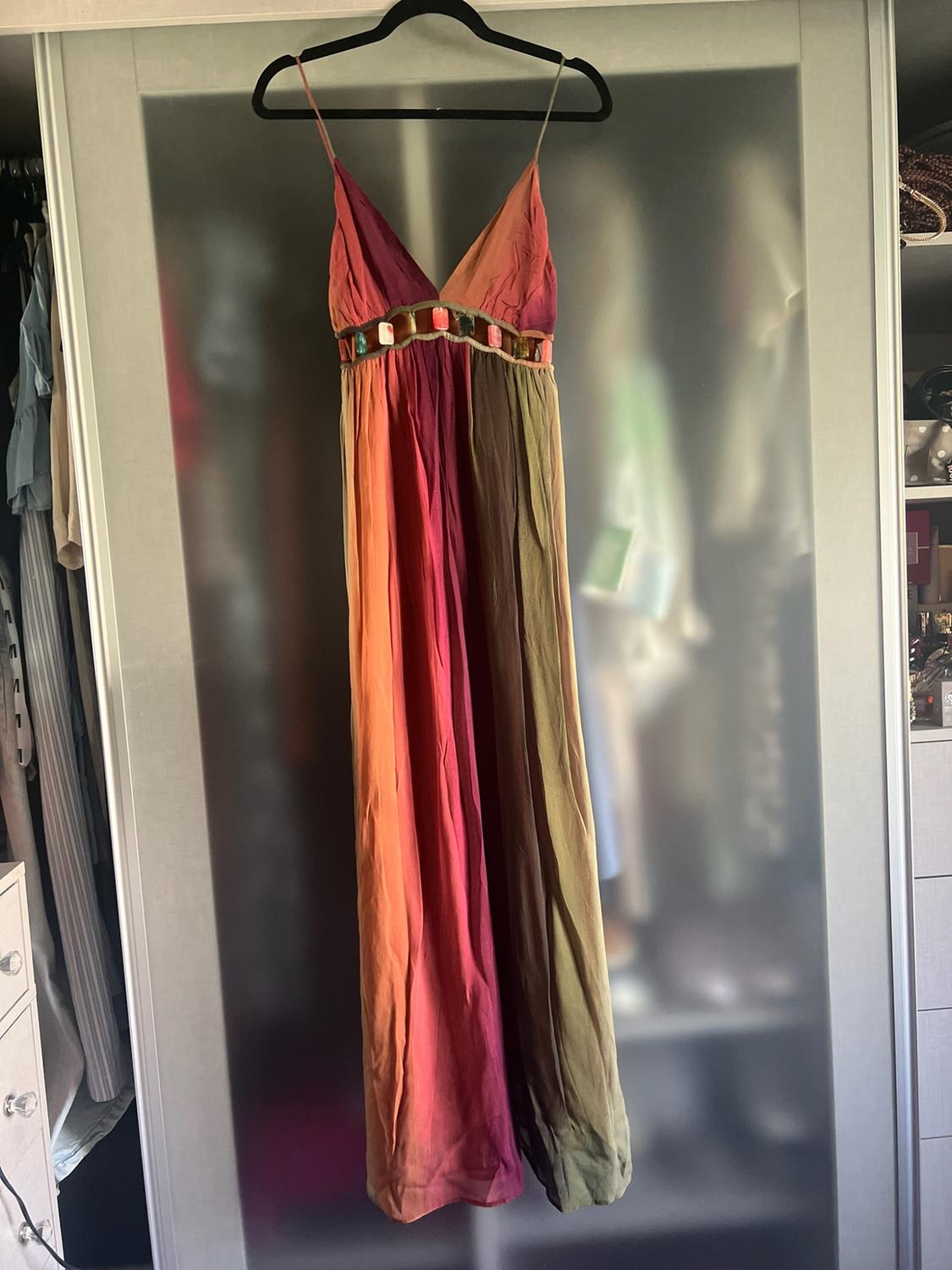 Long strappy dress with a V-neckline, vertical panels in warm tones and beading beneath the bust, hanging in front of a wardrobe.