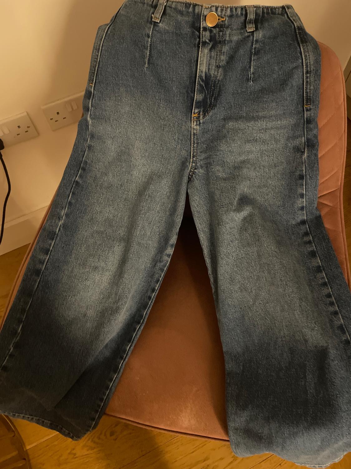 Blue wide-leg jeans on a brown chair, with visible gold button, in a well-lit indoor setting.