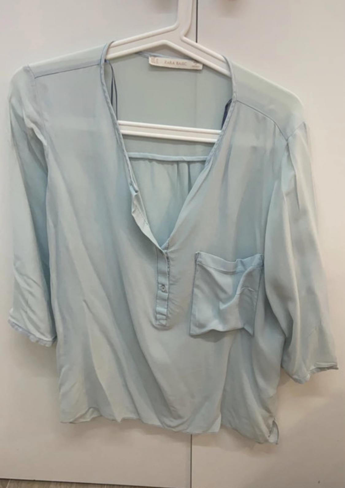 Front view of a light blue blouse with a V-neck and a chest pocket.
