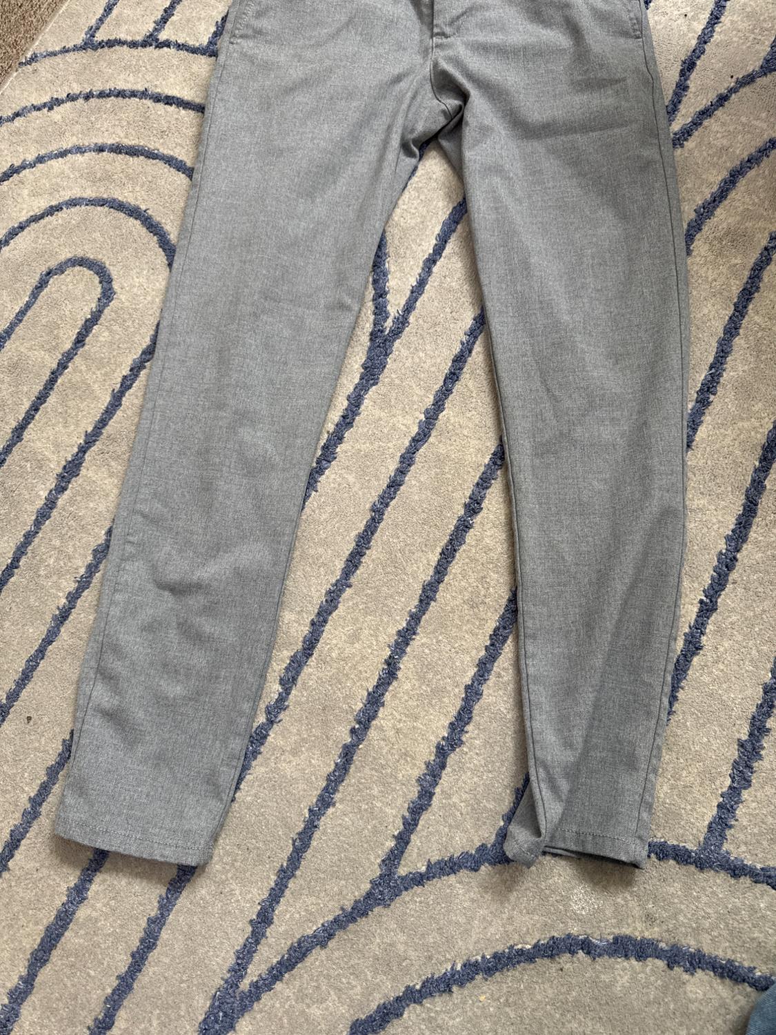 Light grey trousers laid out on a rug with blue curved lines. Relaxed top-down composition with a casual style.