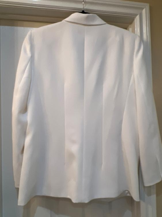 White jacket hanging on a door, seen from behind. Smooth fabric and classic cut with lapel. Illuminated indoor environment.