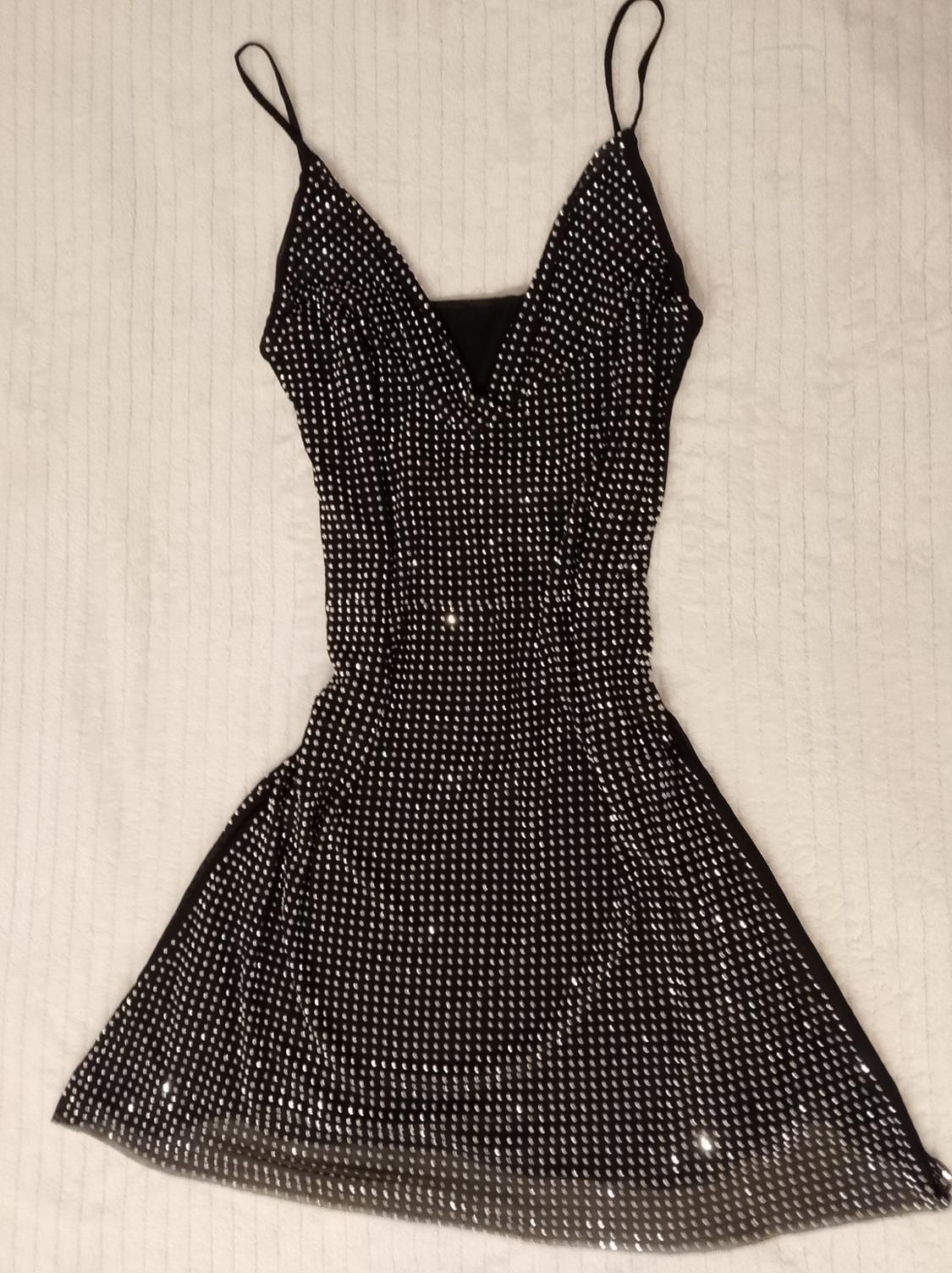 Short black dress with thin straps and a V-neck, covered in glitter, on a white surface with a lined texture.