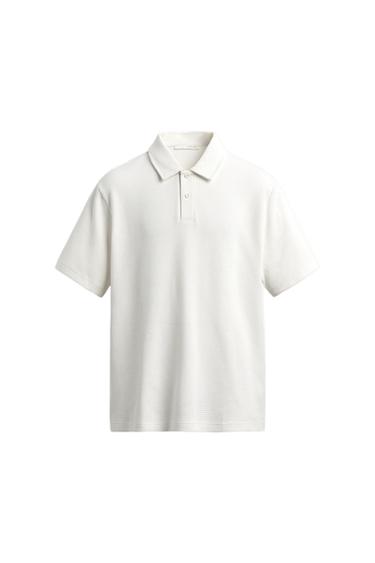 White, short-sleeved polo shirt with textured fabric and a button-down collar. Minimalist and clean composition on a white background.
