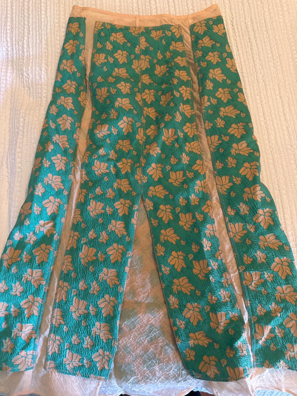 Long green skirt with a beige floral print on a white surface. Textured fabric with a symmetrical design.
