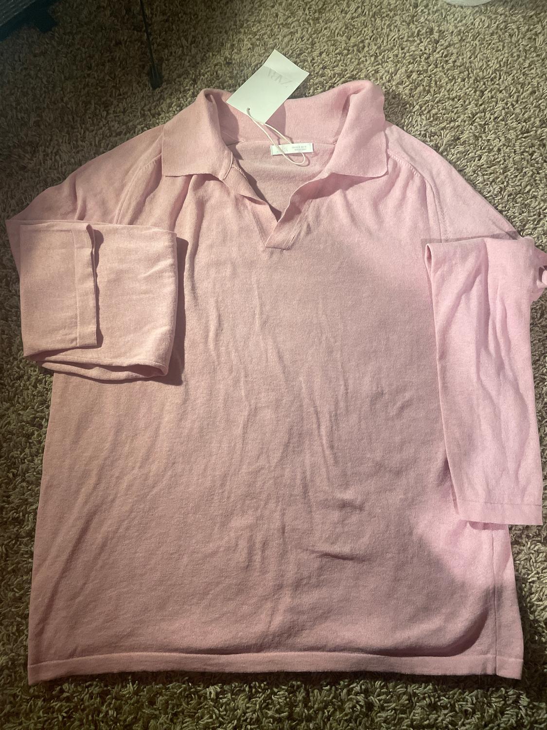 Pink long-sleeved collared shirt, laid on a beige rug. White tag visible on the collar.
