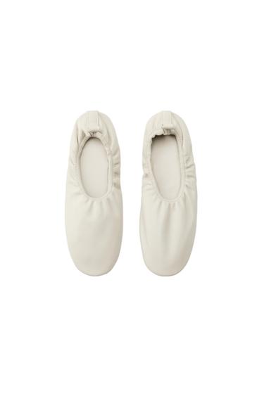 Pair of Ecru ballet flats with elasticated edging and a heel pull tab, photographed from above against a white background.