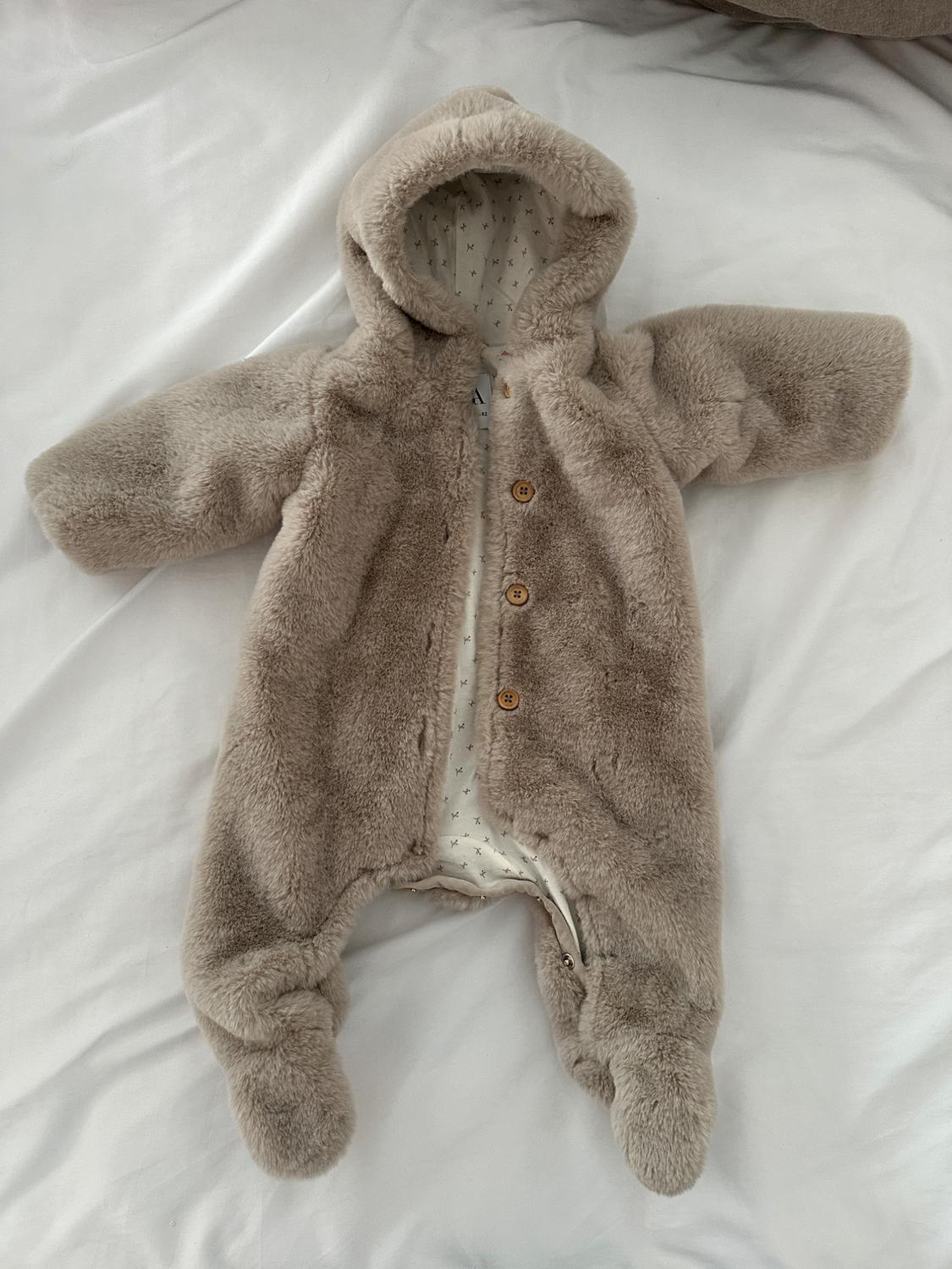 Beige fleece babygrow with hood and wooden buttons, on a white sheet. Interior lining with star print.