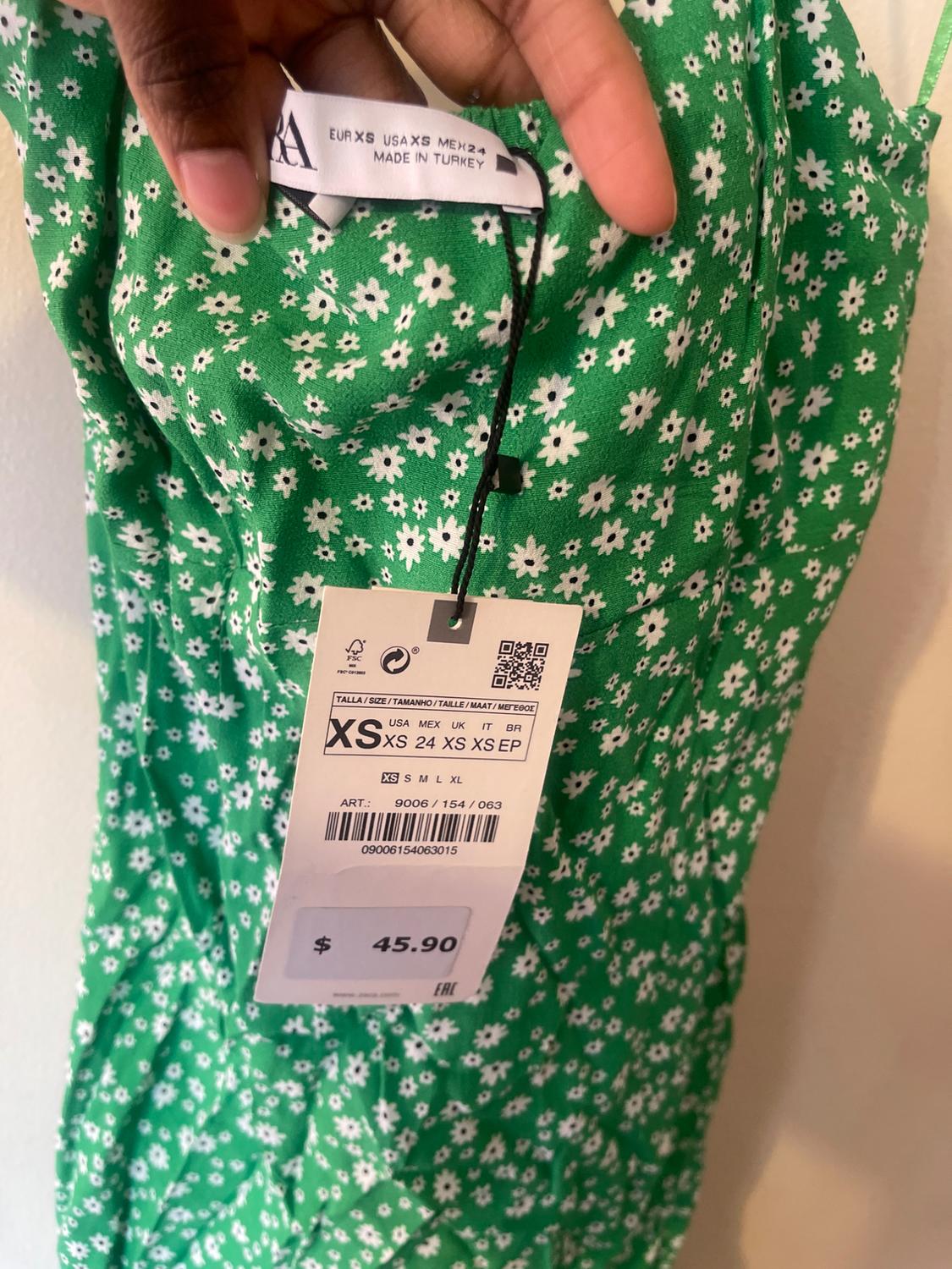 Green dress with white floral print, size XS tag, and price $45.90. Made in Turkey. Hand holding garment.