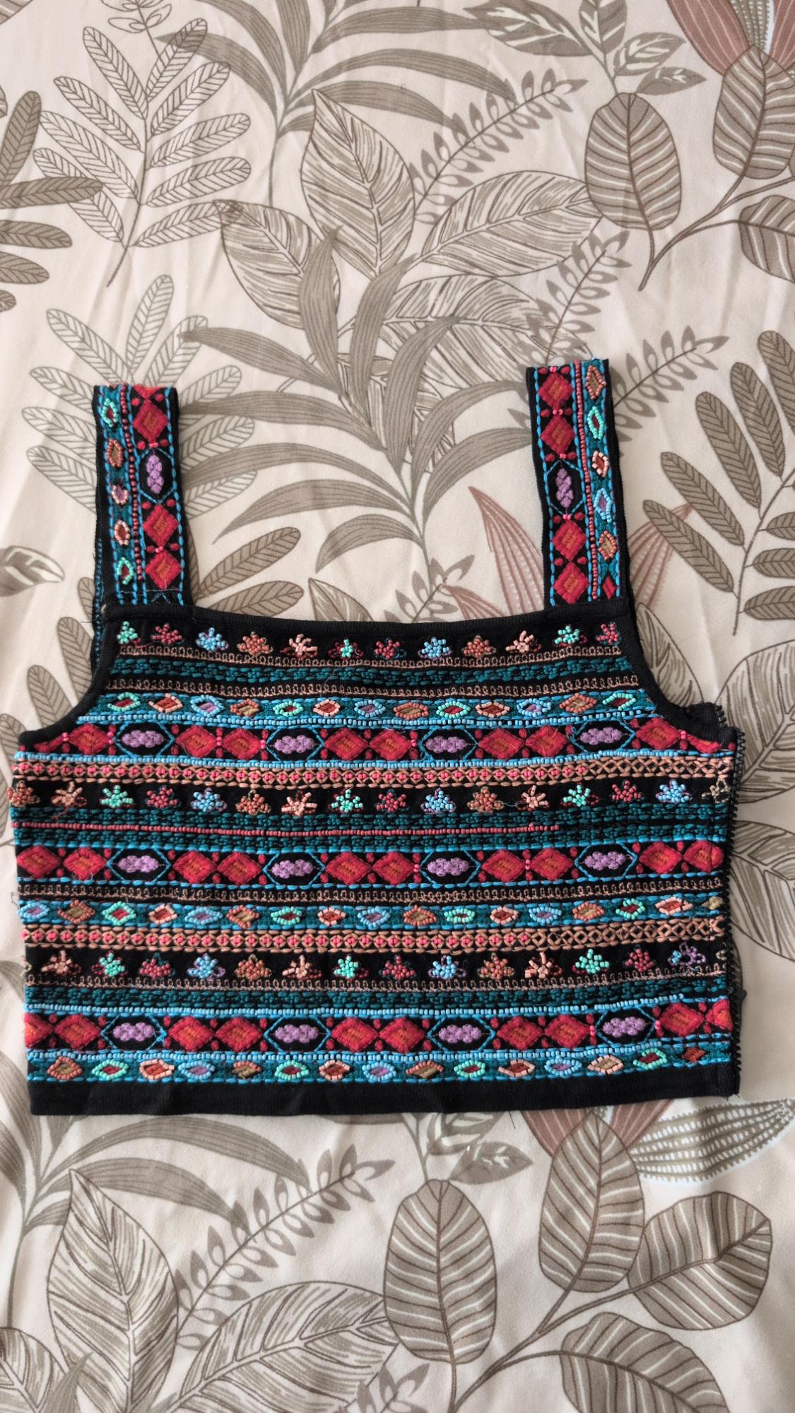 Black cropped tank top with multicolored geometric embroidery, set against a leaf-print fabric.