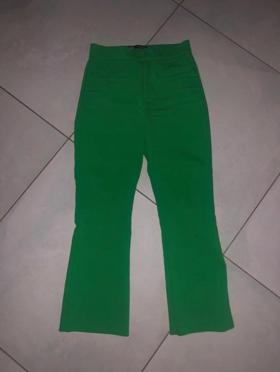 Intense green high-waisted full-length trousers with a slightly flared hem, laid out on a light tiled floor.