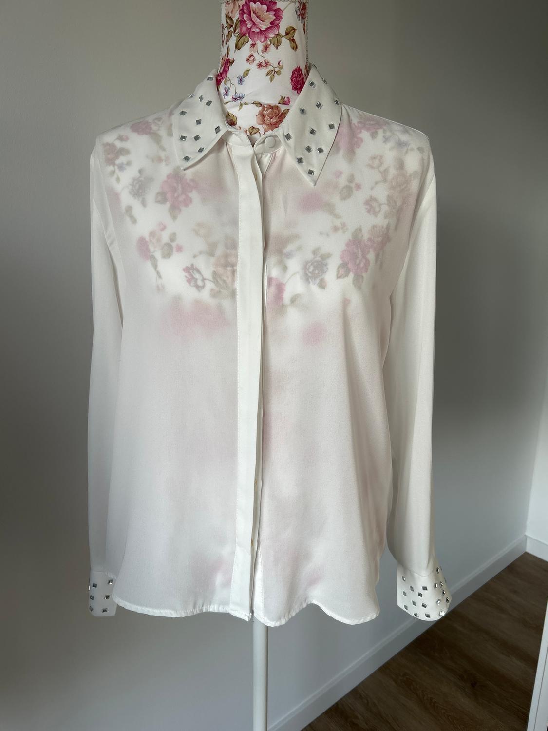 Sheer white blouse with a floral print on a mannequin. Collar and cuffs decorated with small metallic squares. Neutral background.