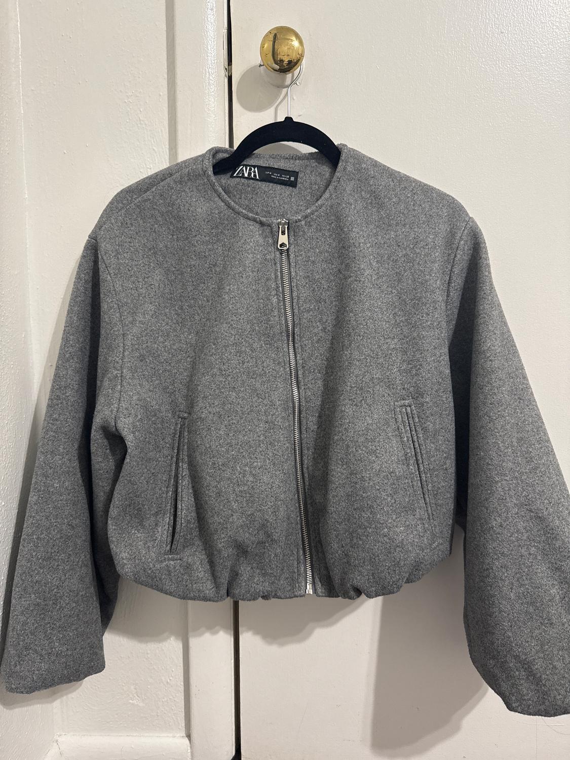Grey zip-up jacket hanging on a black hanger over a white door. Label visible on the collar.